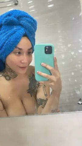 SallyLynn18 takes a mirror selfie in a bathroom, wearing a blue towel wrap on her head and showing off her tattoos.