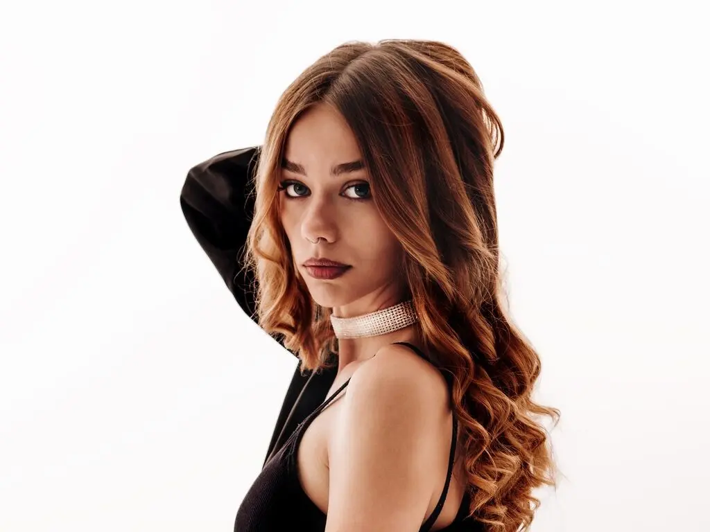 Elegant woman with wavy brown hair wearing a black top and sparkling choker against a white studio background.