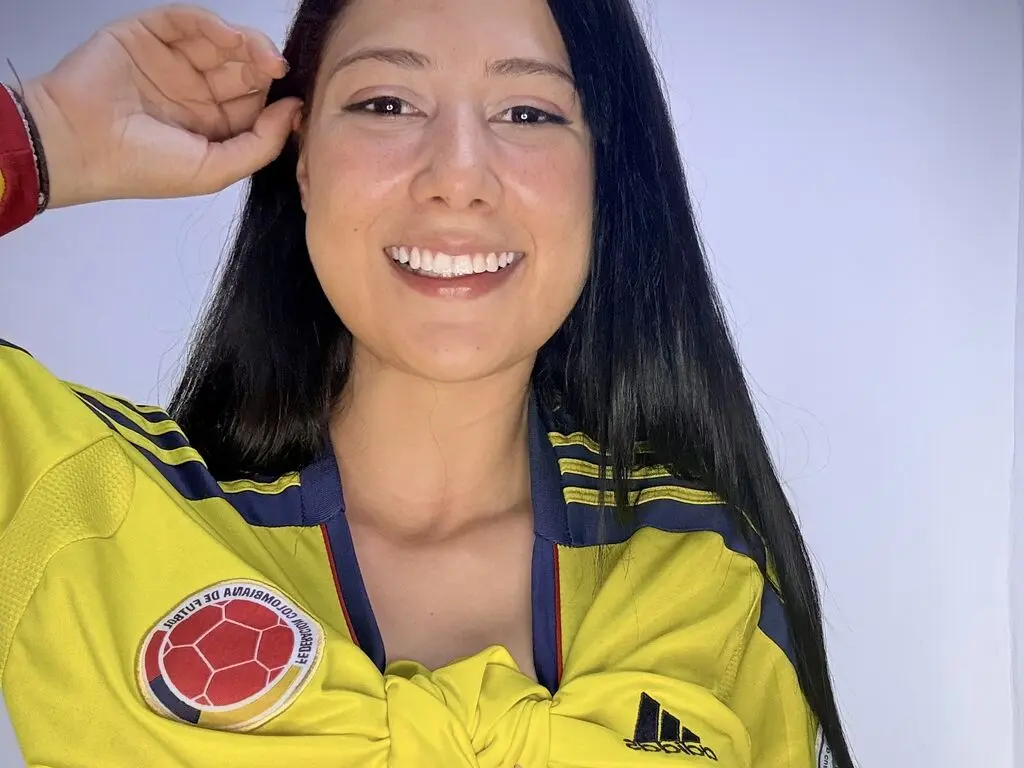 Smiling woman in a yellow Colombia soccer jersey posing happily against a plain background.