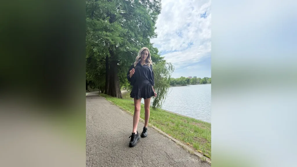 Maddy — MaddyScarlett stands on a paved path in a black mini dress and black boots with trees and a lake in the background.