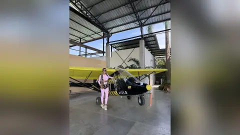 Aleja stands next to a yellow and black light aircraft wearing a pink tank top and pink leggings.