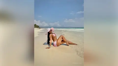 Stylish woman in a pink bikini and sun hat relaxing on a sunny tropical beach.