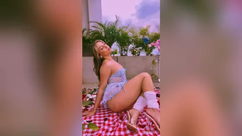 MeganLewit poses outdoors on a red checkered picnic blanket wearing a light blue lace lingerie set and white thigh-high boots.