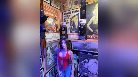 Young woman in a red tank top standing in a vintage retro room filled with classic movie posters.