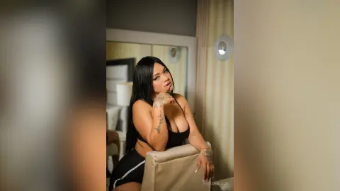 SofiahBlack poses in a black top and shorts, looking at the camera with long dark hair and tattoos on her arms.