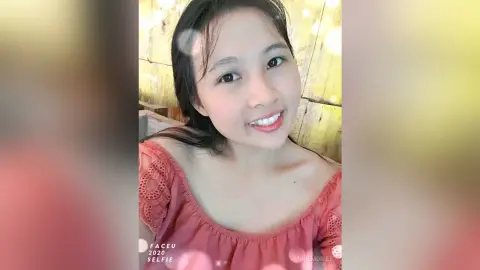 Smiling young woman in a pink lace off-the-shoulder top enjoying a warm, glowing outdoor setting.