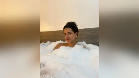 Young woman relaxing in a bubbly white bubble bath in a modern bathroom setting.