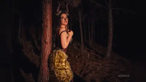 JessieLiu poses in a dark forest wearing a brown furry outfit and dark horns.