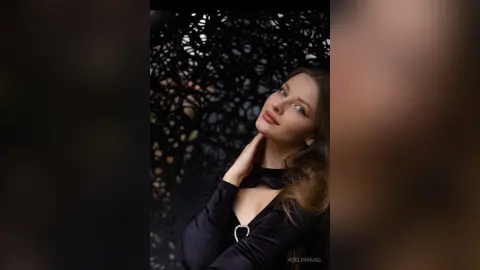 Elegant woman in a black velvet dress posing against a dark, textured floral background with a moody aesthetic.