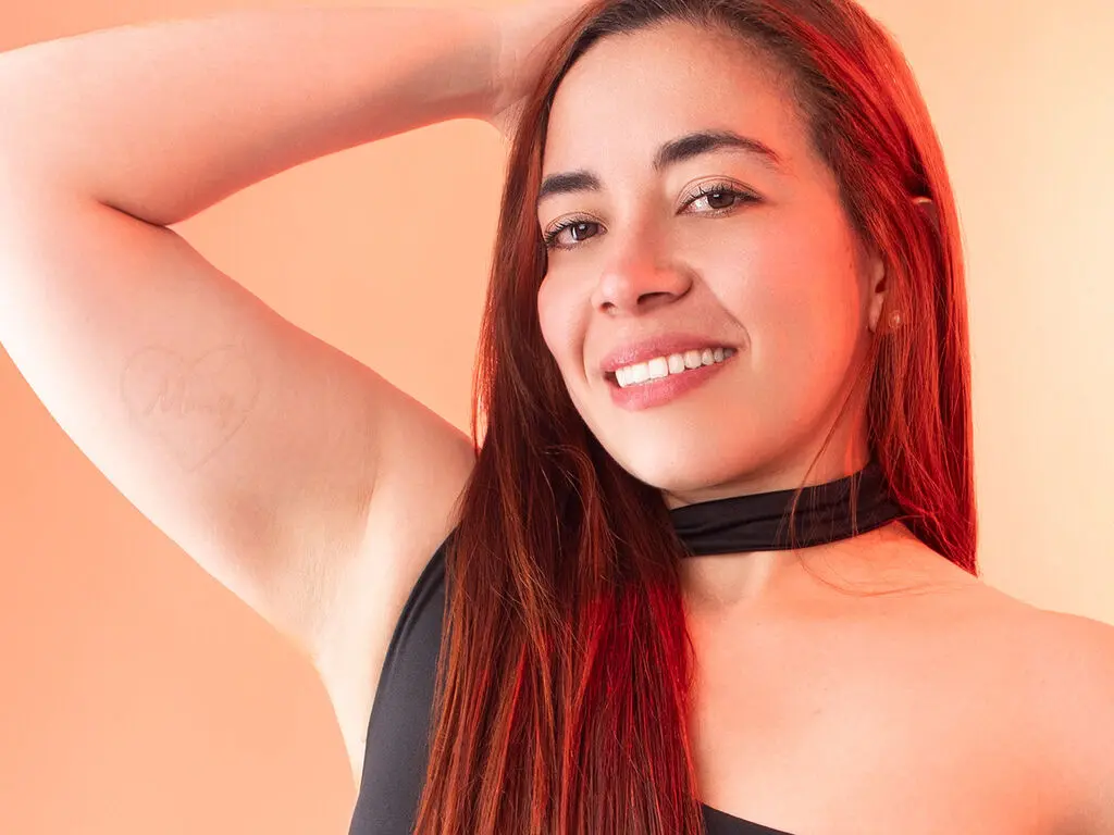 Smiling woman with long brown hair wearing a black halter top against a warm peach background.