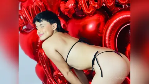 Smiling young woman in black bikini posing amidst red heart balloons for a romantic Valentine's Day mood.