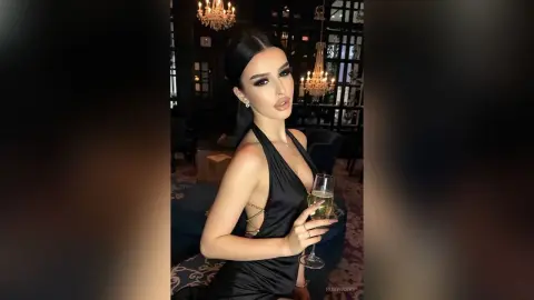 Elegant woman in a black halter dress holding a champagne glass in a luxurious dimly lit lounge.