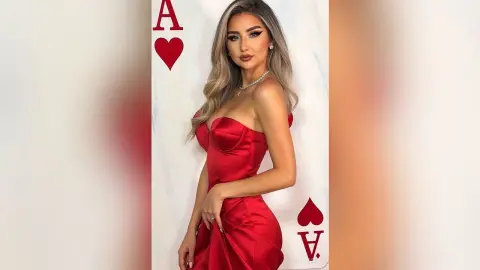 Glamorous woman in a red satin strapless dress posing against a white background with red playing card motifs.