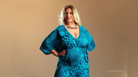Smiling blonde woman in a teal leopard print wrap dress posing against a neutral studio background.