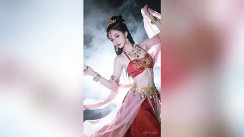 Woman in red traditional belly dance costume with gold jewelry posing in a dreamy, misty setting.