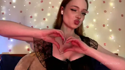 KylieHoneydew pouts her lips and makes a heart shape with her hands while wearing a black lace top.