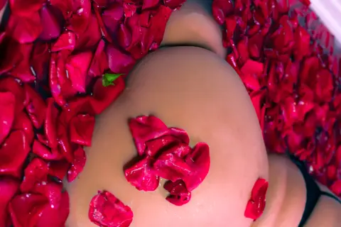Close-up of a person lying in a romantic bath filled with vibrant red rose petals.
