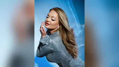 Glamorous woman in a sparkling silver sequin dress posing against a dreamy blue studio background.