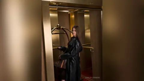 Elegant woman in a black leather coat standing in a luxury gold elevator with a moody, sophisticated vibe.