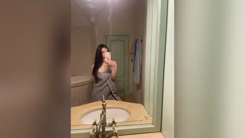 Young woman in a grey towel taking a mirror selfie in a bright, minimalist bathroom.