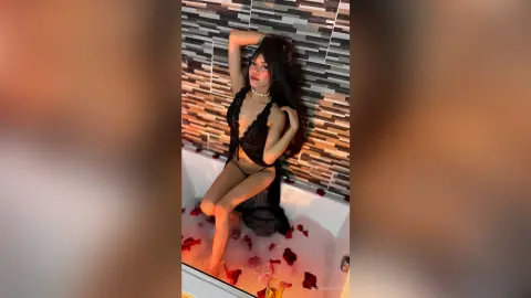 Glamorous woman in a black lace outfit posing in a milky bath against a modern tiled wall.