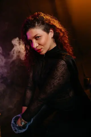 Mysterious woman in a black lace outfit posing amidst dramatic smoke and warm lighting.