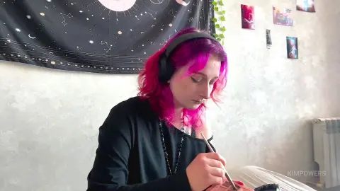 Young woman with pink hair wearing black outfit and headphones, focused on drawing in a cozy bedroom setting.