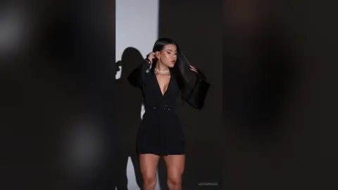 Elegant woman in a chic black mini dress posing against a minimalist studio background with dramatic lighting.