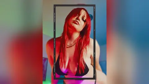 Red-haired woman in a black bikini posing in moody red lighting for a cinematic film frame aesthetic.