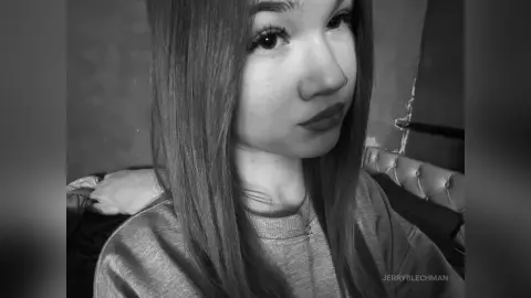 Young woman with long straight hair wearing a casual sweatshirt in a moody black and white portrait.