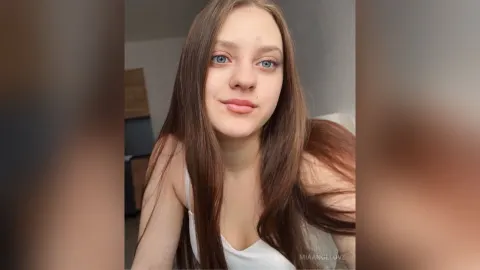 MiaAngelove — MiaAngelove with long brown hair and blue eyes wearing a white tank top.
