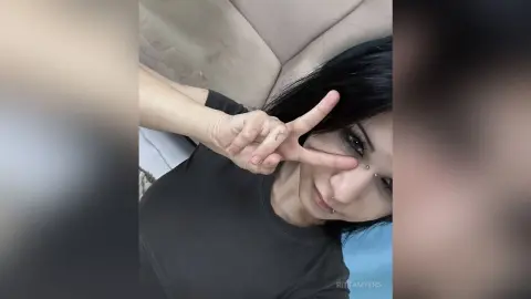 RittaMyers poses with a peace sign near her face, wearing a black t-shirt and showing her long dark hair.
