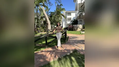 Stylish woman in a lace crop top and white patterned skirt posing on a sunny tropical resort walkway.