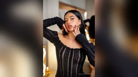 Elegant woman in a black lace long-sleeve dress posing glamorously in a luxury indoor setting.