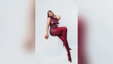 Elegant woman in a burgundy satin dress and matching tights posing confidently against a white studio background.
