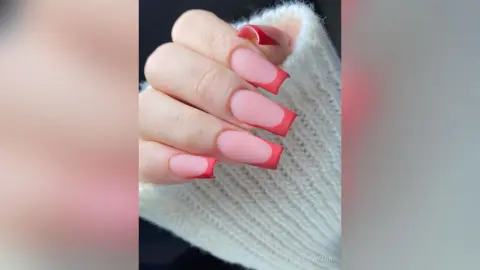 Close-up of elegant pink French tip manicure with red accents on long almond shaped nails.