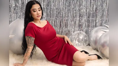 JuliahLewis reclines on a white shag rug wearing a tight red dress against a silver tinsel backdrop.