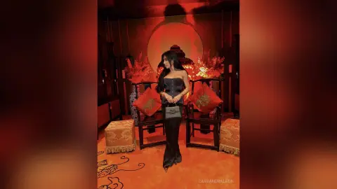 Elegant woman in a black strapless gown posing in a moody, red-lit luxury lounge setting.