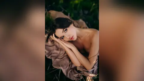 Young woman in a neutral draped outfit relaxing in a lush green garden with a peaceful, serene mood.
