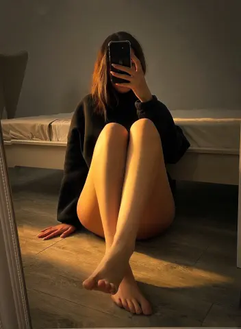 Woman in a cozy black sweater sitting on a floor in warm sunset lighting for a moody aesthetic vibe.