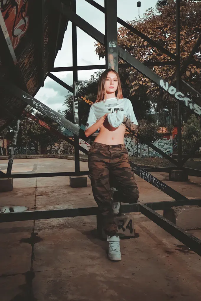 scarletjonessX — Young woman in a white t-shirt and camo pants posing in an urban industrial setting with a moody vibe.