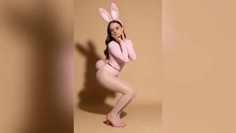 MiaAngelove — MiaAngelove poses in a pink bunny outfit with white tights and bunny ears against a tan background.