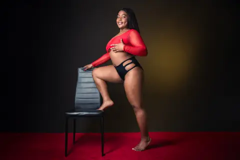 Smiling curvy Black woman in red long-sleeve crop top and black cutout lingerie posing in a studio setting.