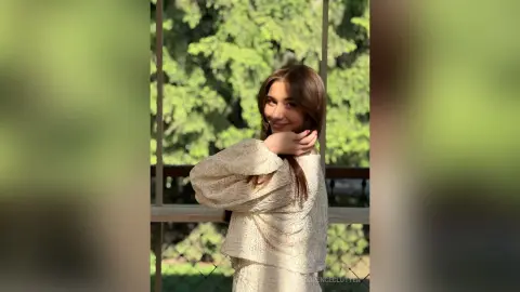 Smiling young woman in a white lace blouse posing in a sunlit garden setting with a dreamy mood.