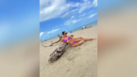 Young woman in a pink bikini relaxing on a sandy beach under a blue sky.