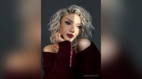 Portrait of a blonde woman in a burgundy sweater with moody lighting and elegant makeup.