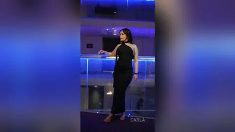 Elegant woman in a sleek black evening gown posing on a balcony under moody blue lighting.