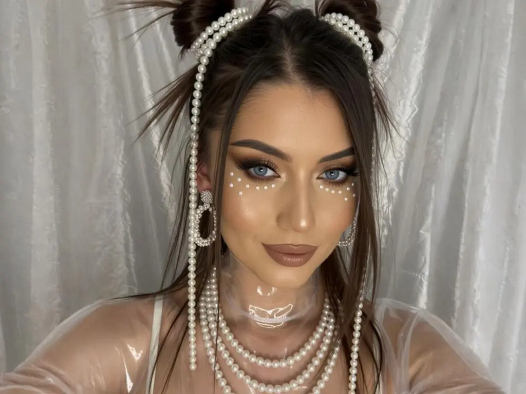 Glamorous woman with pearl face gems and pearl accessories posing against a white curtain backdrop.