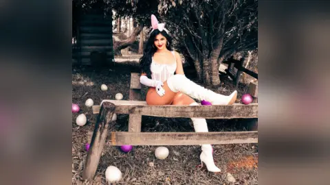 Woman in white bunny costume and boots sitting on a wooden bench in a whimsical forest setting.