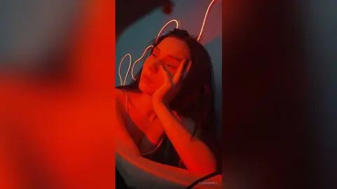 Moody portrait of a young woman in a white tank top under warm red neon lighting.